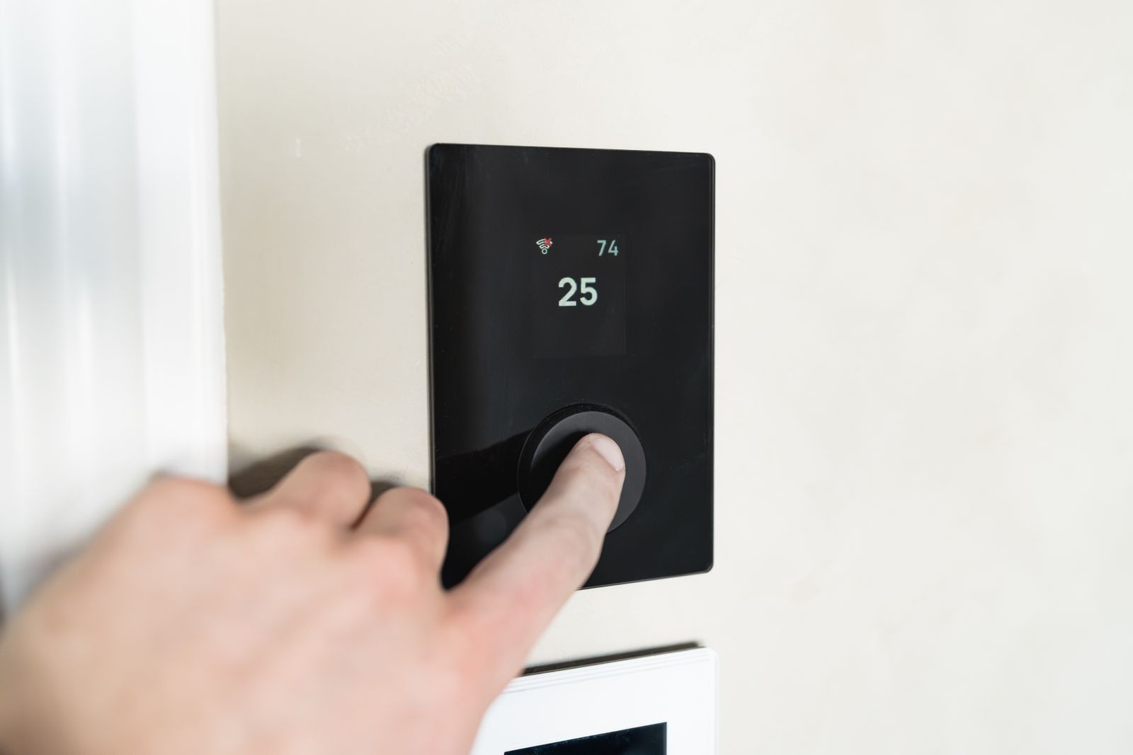 A hand adjusting a modern smart thermostat on a wall